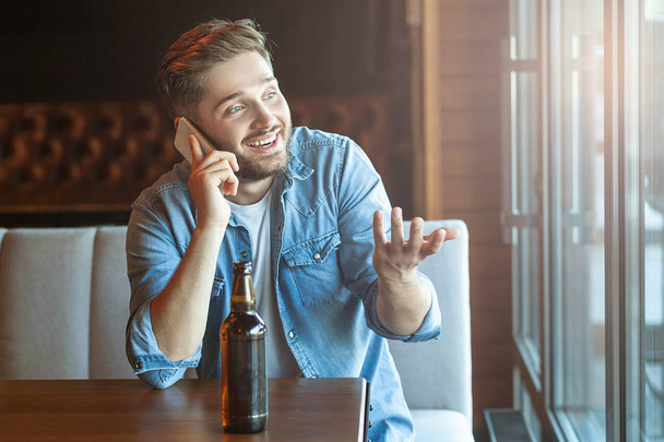 happy man sitting in pub drinking beer and talking on smartphone - Photo, image