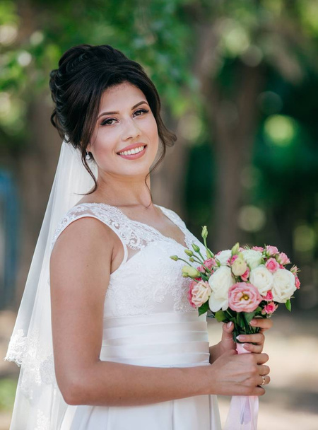 Krásná mladá nevěsta v bílých svatebních šatech pózuje v parku  - Fotografie, Obrázek
