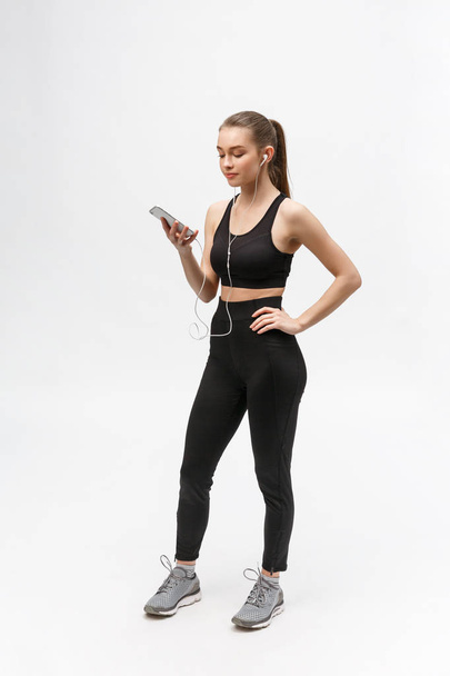Sport woman. Young beautiful woman in sport clothes. Portrait full length sitting in headphones listening music. - Zdjęcie, obraz