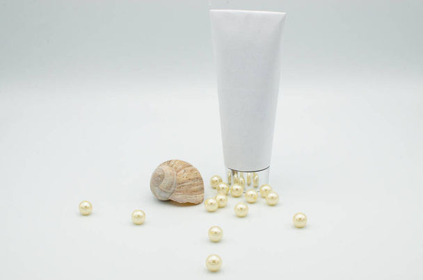 Cosméticos brancos ou tubo de medicina com uma concha e pérolas marinhas isoladas em um fundo branco
 - Foto, Imagem