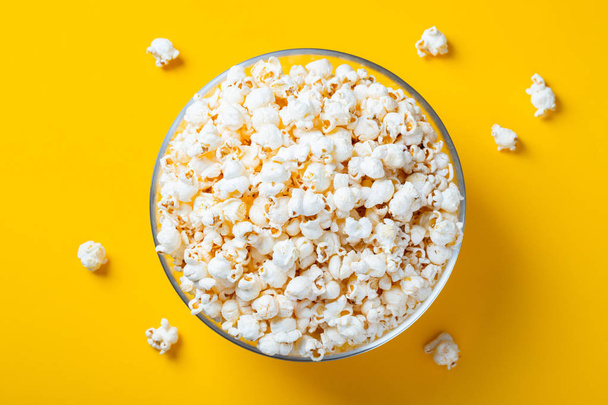 Glass bowl with salted popcorn on yellow background. Top view with copy space. Flat lay. - Photo, image