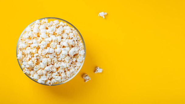 Glass bowl with salted popcorn on yellow background. Top view with copy space. Flat lay - Φωτογραφία, εικόνα