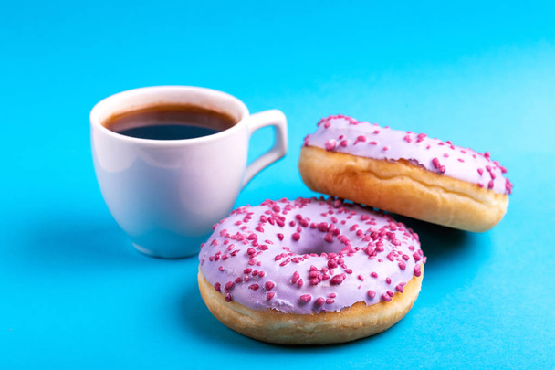 Two tasty lilac donuts with sprinkle and cup of strong coffee on bright blue background. Unhealthy, but delicious sweets. Copy space. Horizontal view - Φωτογραφία, εικόνα