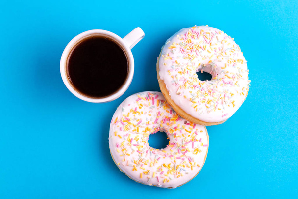 Two delicious vanilla donuts with sprinkle and cup of coffee on bright blue background. Unhealthy, but tasty sweets. Copy space. Top view - Foto, immagini