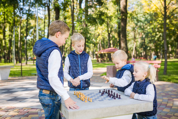 The topic children learning, logical development, mind and math, miscalculation moves advance. large family brothers and sister Caucasian boys and girl playing chess park bright sunny weather autumn. - Photo, Image