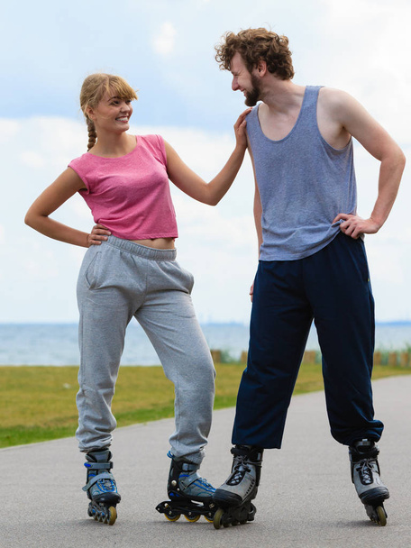 Active lifestyle people and freedom concept. Young fit couple on roller skates riding outdoors on sea coast, woman and man enjoying time together. - Фото, зображення