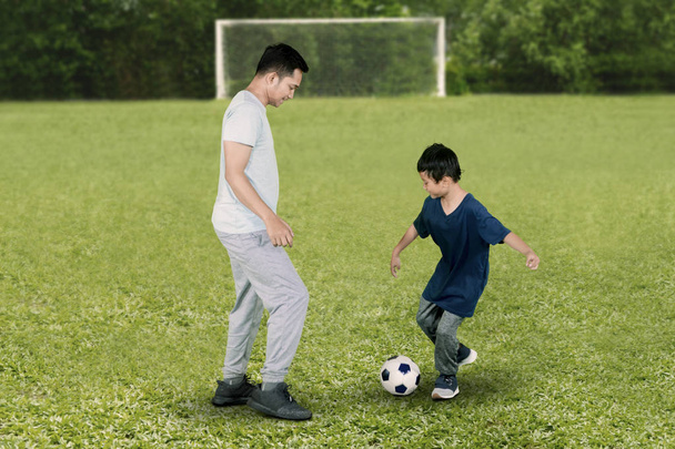 Picture of a little boy and his father looks happy while playing football in the field - Foto, Imagem