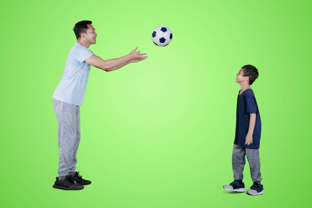 Picture of young man throwing a soccer ball to his son while playing in the studio with green screen - Foto, Imagen