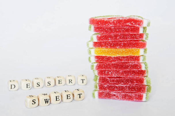 Schludny stos Marmolada położony jest na białej powierzchni. W pobliżu składają słowa z liter: cukru i deser. Słodycze.                                - Zdjęcie, obraz