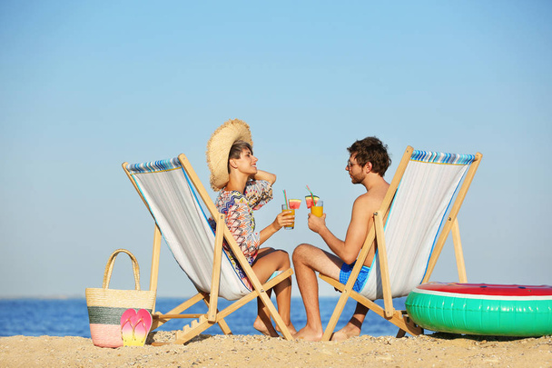 Young couple with cocktails in beach chairs at seacoast - Valokuva, kuva