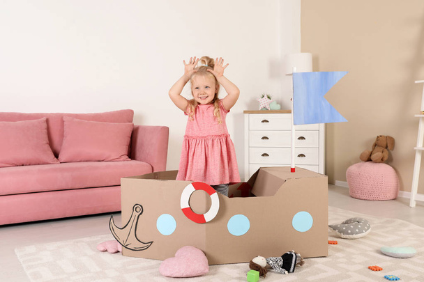 Cute little girl playing with cardboard ship at home - Fotoğraf, Görsel