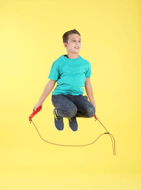 Full length portrait of boy jumping rope on color background - 写真・画像