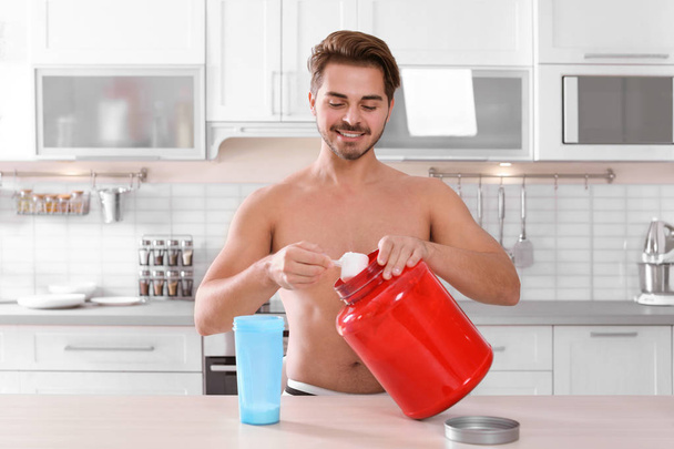 Young shirtless man preparing protein shake at table in kitchen - Valokuva, kuva