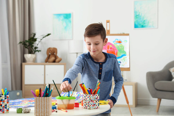 Дівчина малює за столом і хлопчик біля мольберта в приміщенні. Креативні діти
 - Фото, зображення