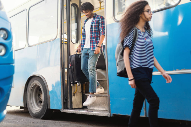 junger Afroamerikaner steigt mit Gepäck in der Hand aus dem Bus. - Foto, Bild