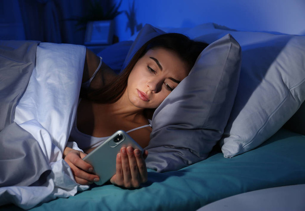 Young woman with mobile phone at night. Bedtime - Foto, afbeelding