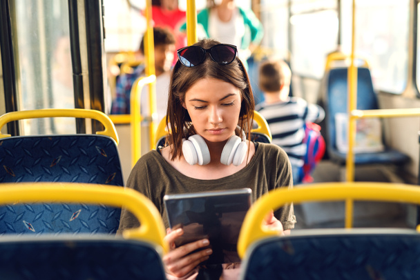 Pretty young girl with headphones sitting in a bus and watching tablet. - Photo, Image