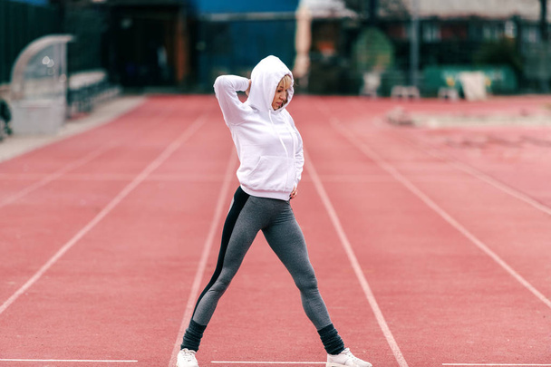 Fit mooie sportieve vrouw met hoodie bij het doen van de warming-up oefeningen op het circuit. Volledige lengte. - Foto, afbeelding