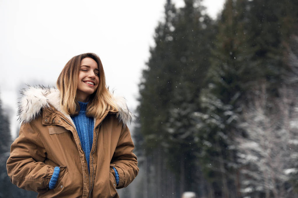 Young woman in warm clothes near forest, space for text. Winter vacation - Photo, Image