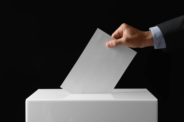 Man putting his vote into ballot box on black background, closeup - Фото, изображение