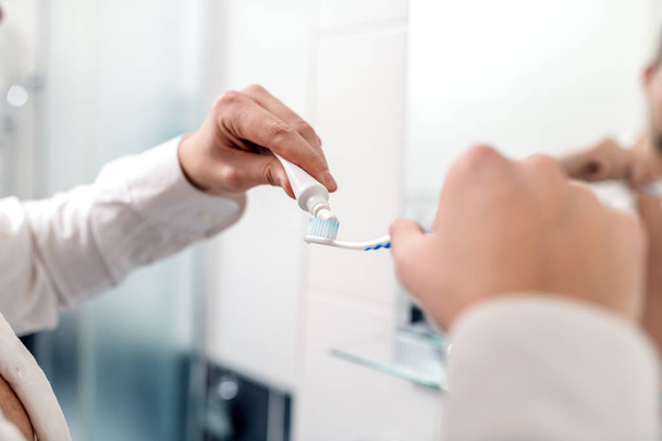 Close up of businessman putting toothpaste on the brush while standing in bathroom. Morning routine concept. - Foto, Imagem