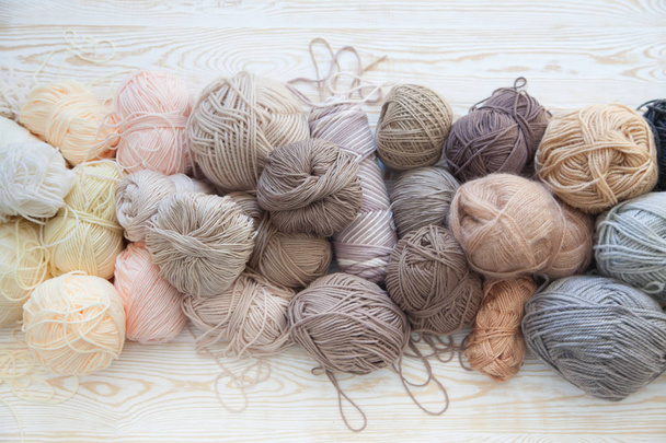 The yarn is beige, brown, gray and white. The background is aged wood. Knitting needles, scissors, coffee, knitting, knitted fabric. - Zdjęcie, obraz