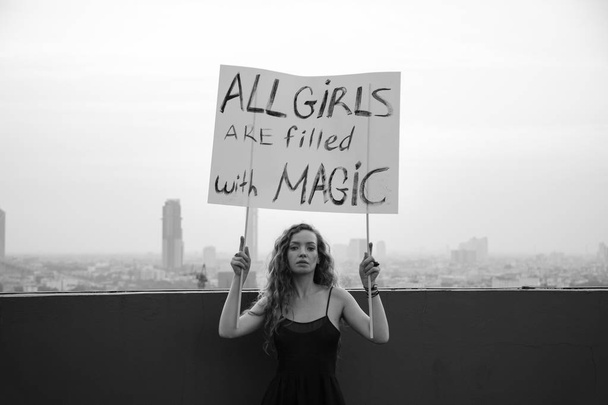 The girl stands on the roof with a poster "All girls are filled with Magic" International Womens Day concept - Photo, Image