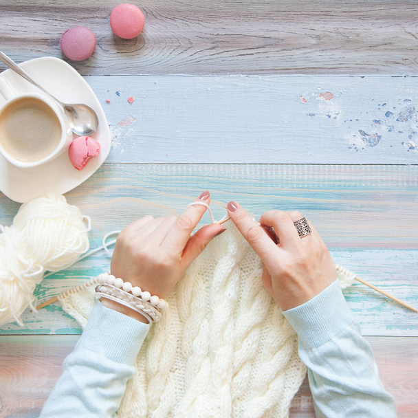 Knitting with knitting needles. White knitted fabric. Coffee Americano. Light aged background. - Valokuva, kuva