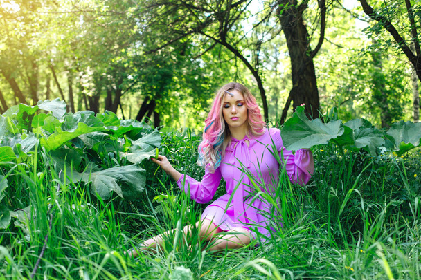 Fairy girl unicorn with rainbow hair and shiny makeup sitting on the grass in the forest. - Foto, Imagem