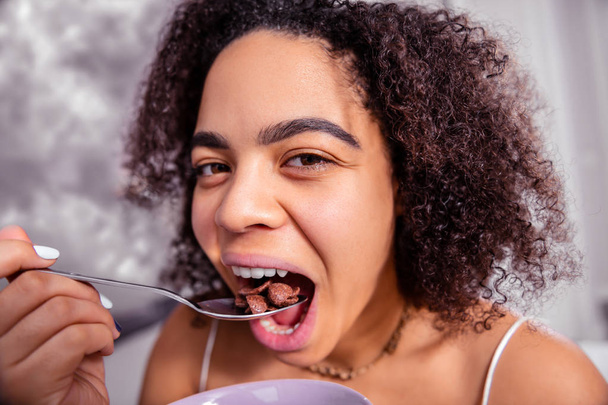 Attractive dark-haired lady throwing chocolate cereals in her open mouth - 写真・画像