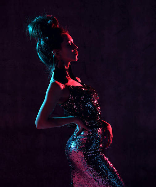Beautiful fashion sexy brunette woman posing in blue and pink neon light in fashion gold sparkle dress on dark background - 写真・画像
