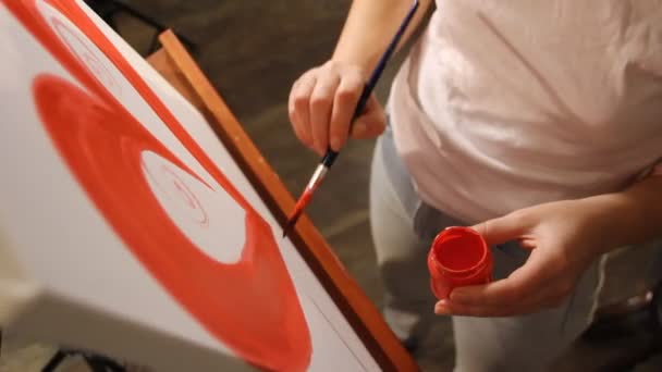 Close-up van de hand van de kunstenaar schilderen een rood hart op een doek op de ezel - Video