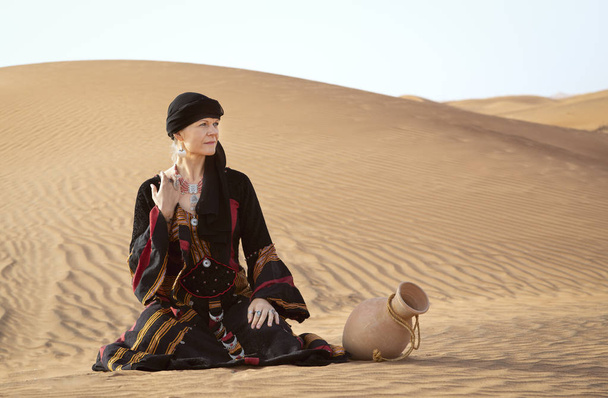middle aged woman in yemeni traditional dress in desert with water dish - Фото, зображення
