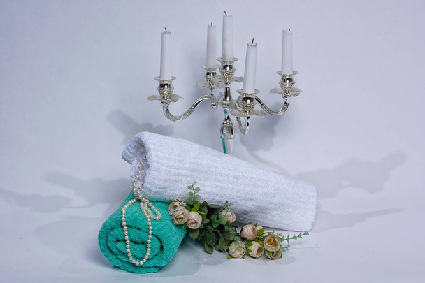 Turquoise and white towel on a white background. Roses are lying on the towel. Candles and towels on a white background. Hanging beads. The texture of the fabric. - Photo, Image