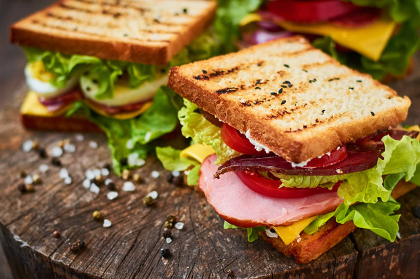 Домашний сэндвич с ветчиной, салатом, сыром и помидорами на деревянном фоне
 - Фото, изображение