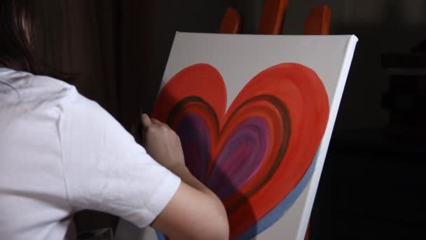 close up of woman artist painting a big red heart on the easel in her studio in the dark black background - Footage, Video