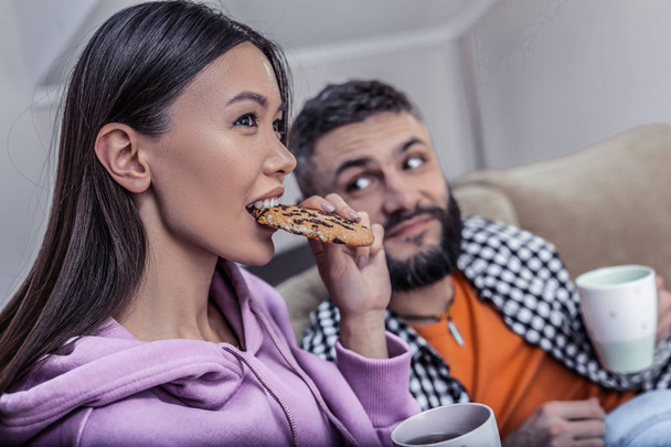 Cute loving couple eating cookies and drinking tea in front of TV - Fotografie, Obrázek