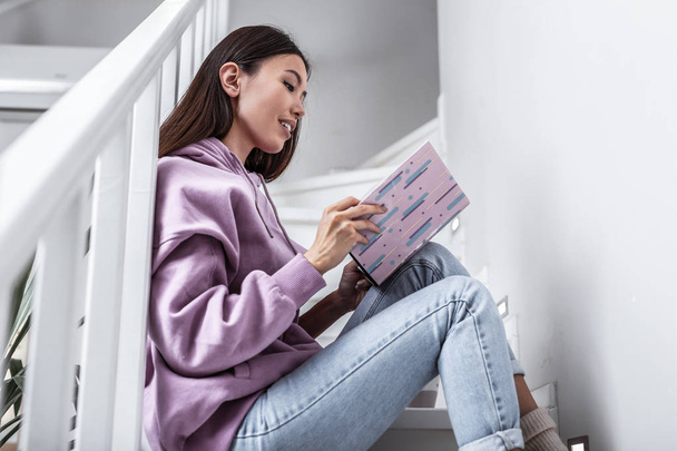 Appealing woman sitting on stairs while reading interesting book - Фото, изображение