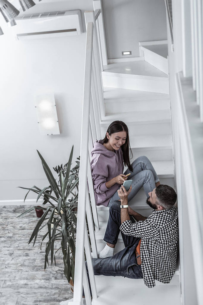 Молода стильна пара сидить на сходах у своєму світлому просторому будинку
 - Фото, зображення