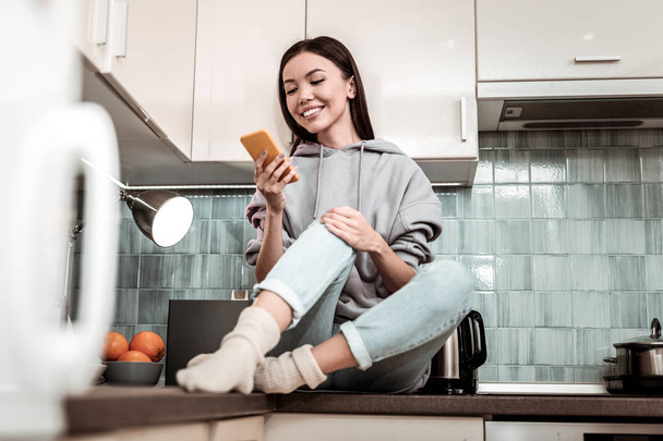 Dark-haired woman wearing jeans and warm socks chilling in kitchen - Foto, Bild