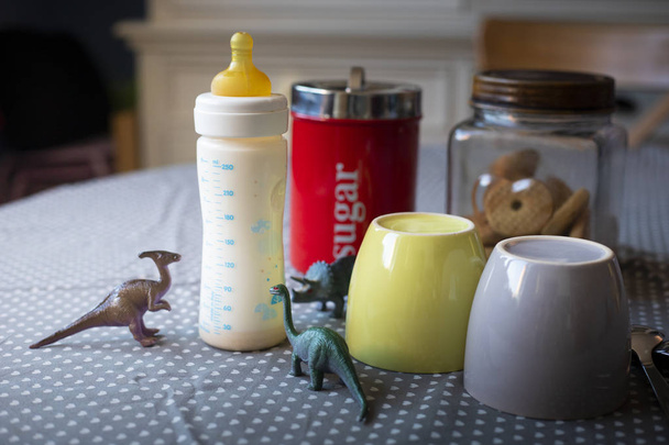 mesa de desayuno listo con tazas y un biberón con juguetes de dinosaurios revelando la presencia de un niño
. - Foto, Imagen