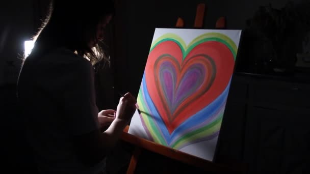 κοντινό πλάνο γυναίκα καλλιτέχνης ζωγραφική μια μεγάλη κόκκινη καρδιά στο καβαλέτο στο ατελιέ της στο σκούρο μαύρο φόντο - Πλάνα, βίντεο