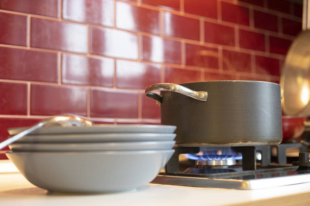 grauer Kochtopf auf Gasherd mit Dampfauslass und blaues Geschirr an der Seite in roter weinroter klassischer Küche. Nahaufnahme. - Foto, Bild