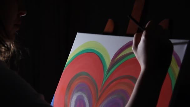 zbliżenie kobieta artysta malarstwo duże czerwone serce na sztalugach w jej pracowni na ciemnym tle czarny - Materiał filmowy, wideo