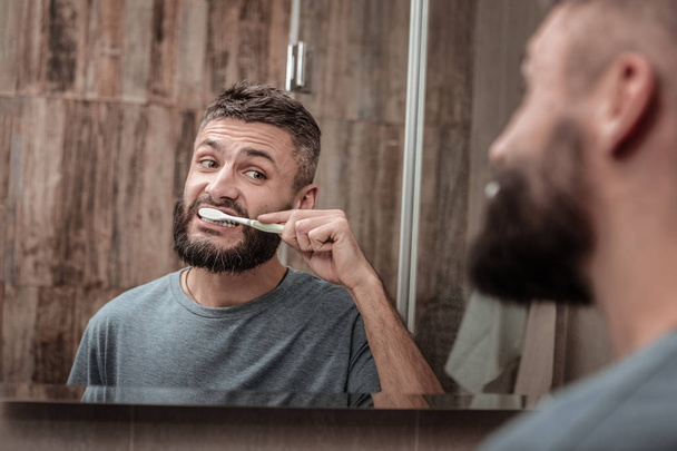 Dark-eyed husband looking into mirror while brushing his teeth - Zdjęcie, obraz