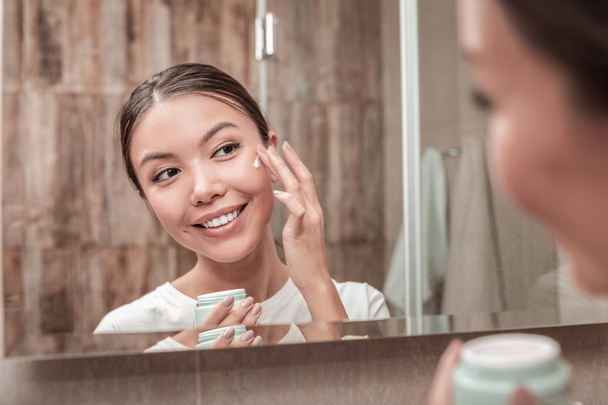Pleasant appealing woman using face cream in the morning - Фото, зображення
