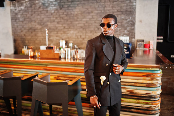 Stylish african american gentleman in elegant black jacket and sunglasses, holding retro walking stick as cane flask or tippling cane with golden diamond ball handle. Rich fashionable afro man. - Valokuva, kuva