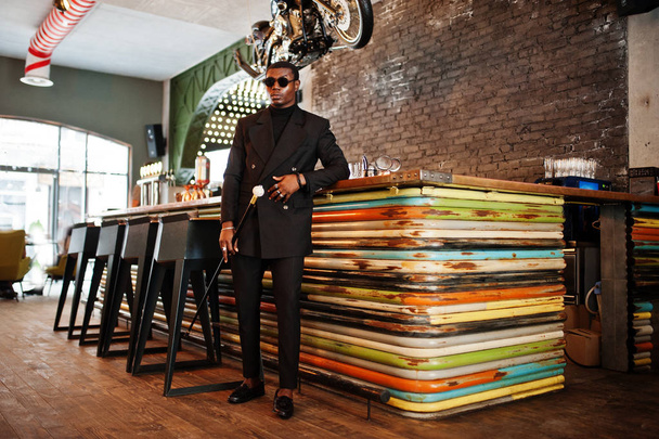 Stylish african american gentleman in elegant black jacket and sunglasses, holding retro walking stick as cane flask or tippling cane with golden diamond ball handle. Rich fashionable afro man. - Zdjęcie, obraz