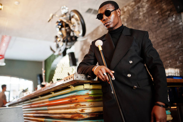 Stylish african american gentleman in elegant black jacket and sunglasses, holding retro walking stick as cane flask or tippling cane with golden diamond ball handle. Rich fashionable afro man. - Фото, изображение