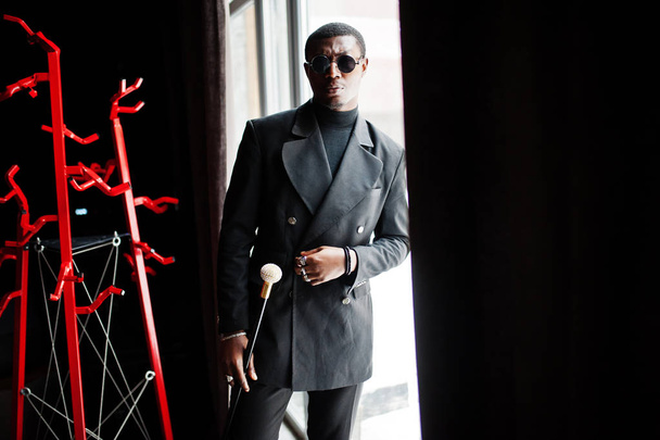 Stylish african american gentleman in elegant black jacket and sunglasses, holding retro walking stick as cane flask or tippling cane with golden diamond ball handle. Rich fashionable afro man. - Foto, immagini